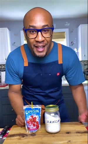 A close-up of Chef Evan leaning into the camera, with a Capri Sun juice pouch and mason jar of ranch dressing in front of him